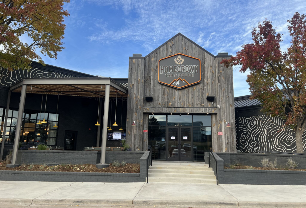 The outside of a brewery. The building is made out of rustic wood. The sign above the door says "Homegrown Tap and Dough"