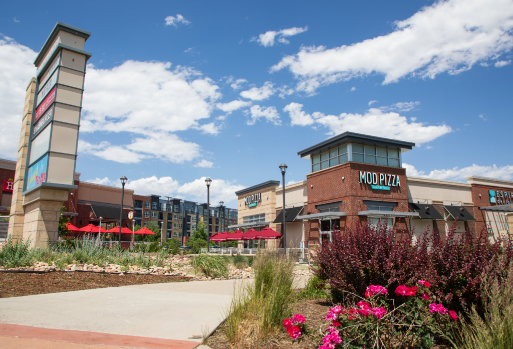 A mixed use area with restaurants and businesses. There are flowers and apartments in the background.